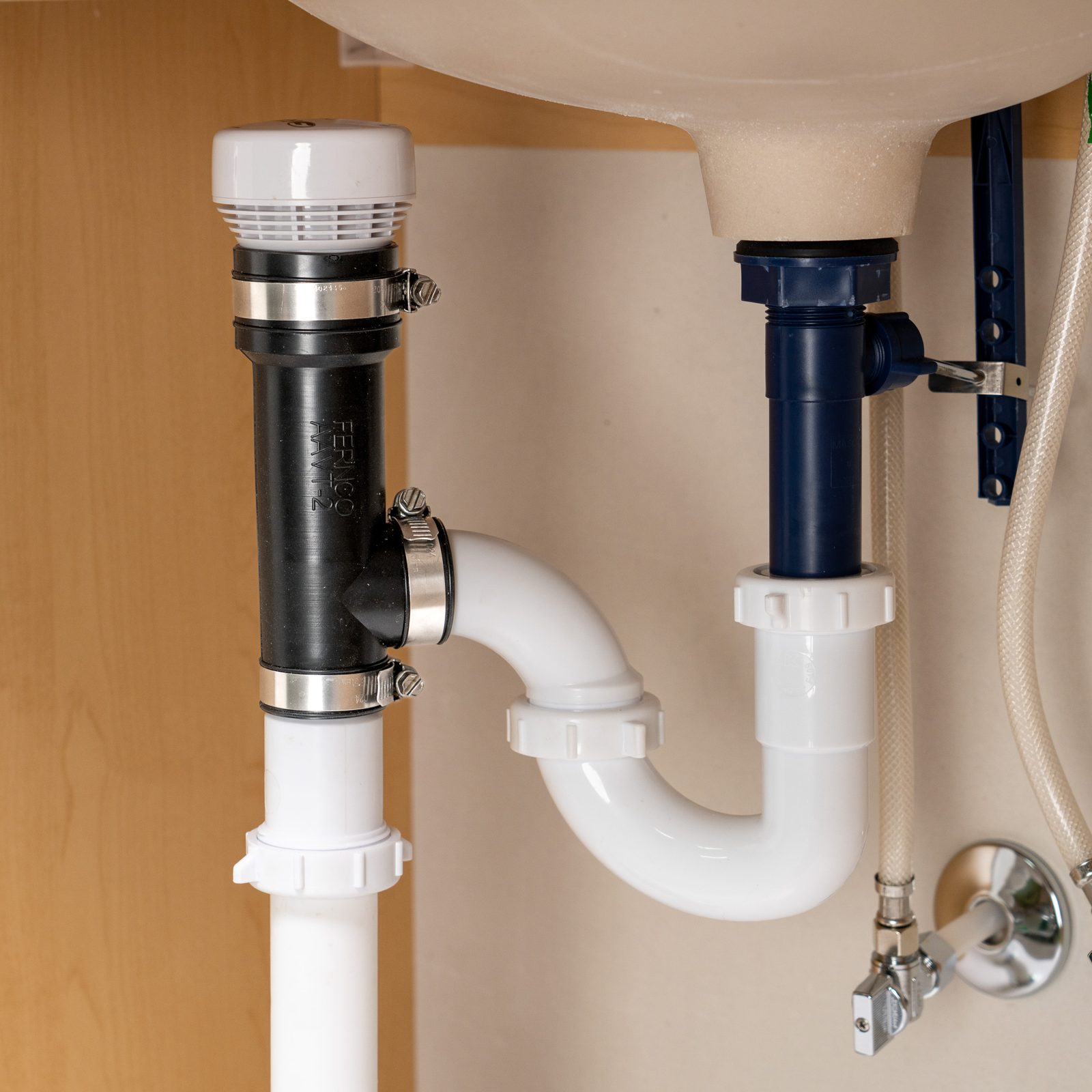 Fernco bottom outlet AAV kit installed on a 1.5 inch tubular drain under a bathroom sink, next to the P-trap