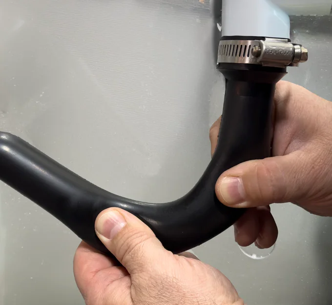 Hand squeezing the flexible condensate trap, clamped to the drain at one end