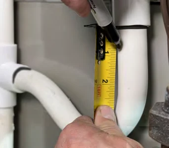 Measuring down from the first mark on the PVC drain pipe with a tape measure