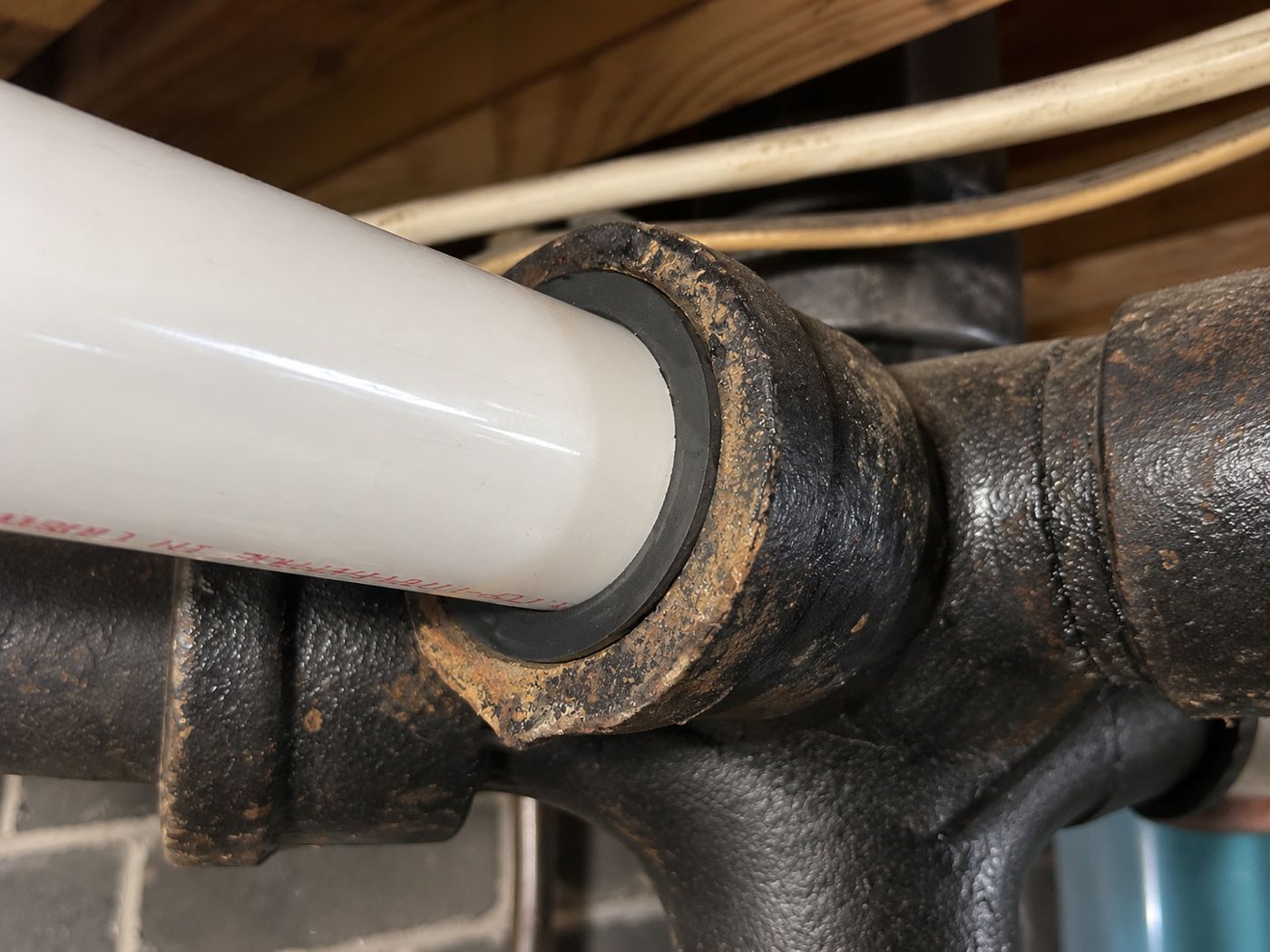 Fernco Donut sealing white PVC pipe into an old cast iron hub under a basement floor
