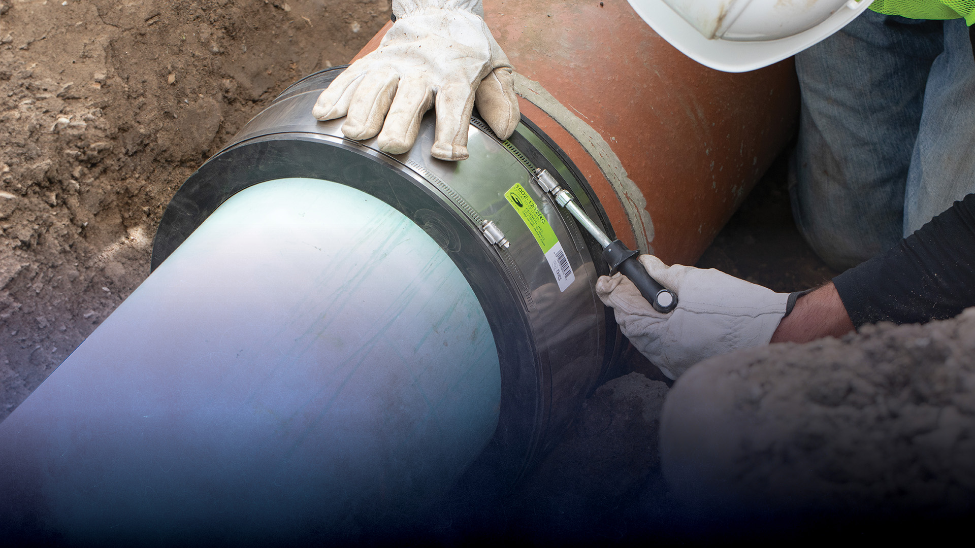 A contractor tightening a Fernco Strong Back RC coupling joining PVC to clay pipe in a trench