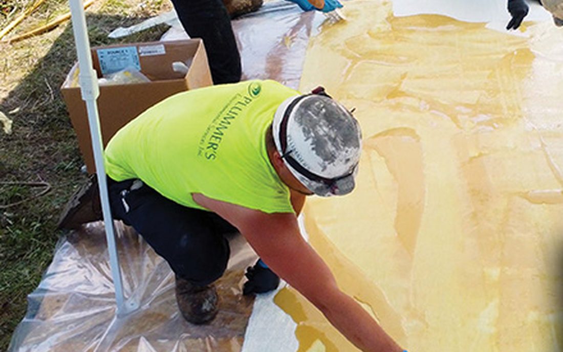 A crew spreading resin across a large fiberglass mat on a ground sheet