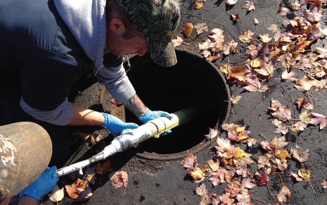 A technician feeding a wrapped packer into a manhole