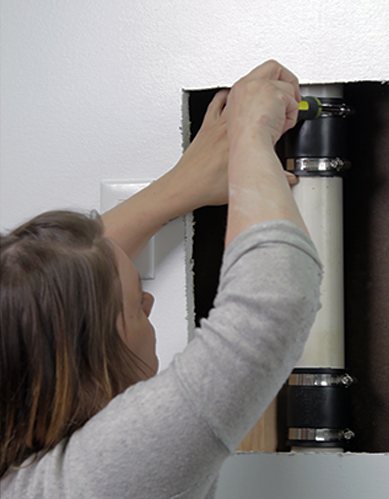 Tightening a QwikFix coupling clamp on a pipe inside the wall with a screwdriver