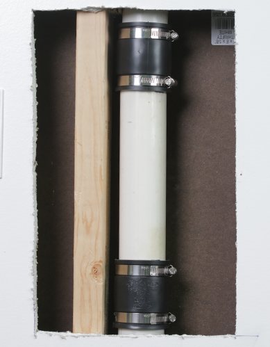 A finished QwikFix repair: new PVC pipe with a coupling at each end, between two studs