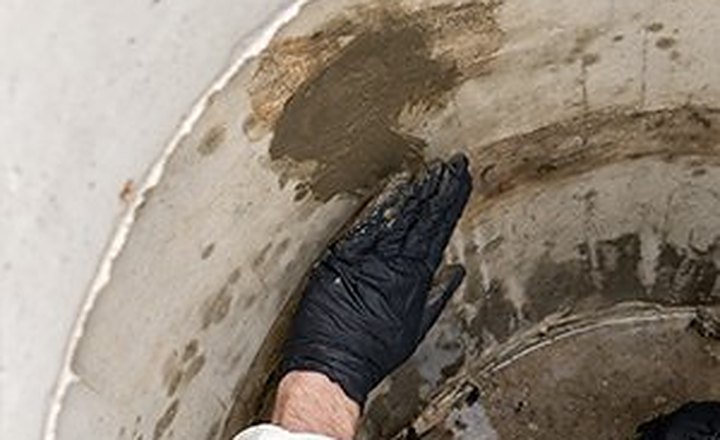 Gloved hand pressing patching material over a wet spot on a concrete manhole wall