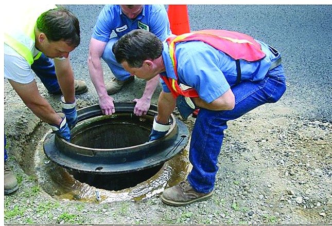Three workers lowering a manhole frame onto X-Seal