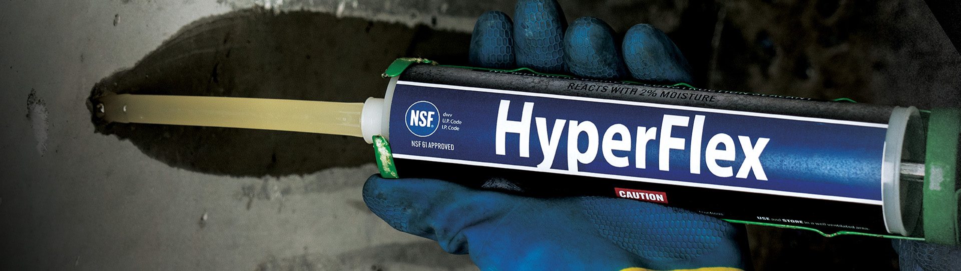 A gloved hand pressing a HyperFlex tube nozzle into a hole at a leaking crack in a concrete wall