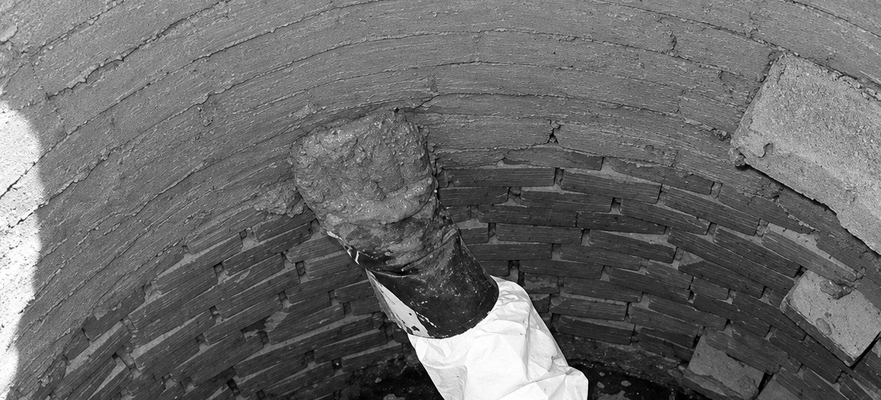 A gloved hand pressing leak-stop cement into a brick manhole wall