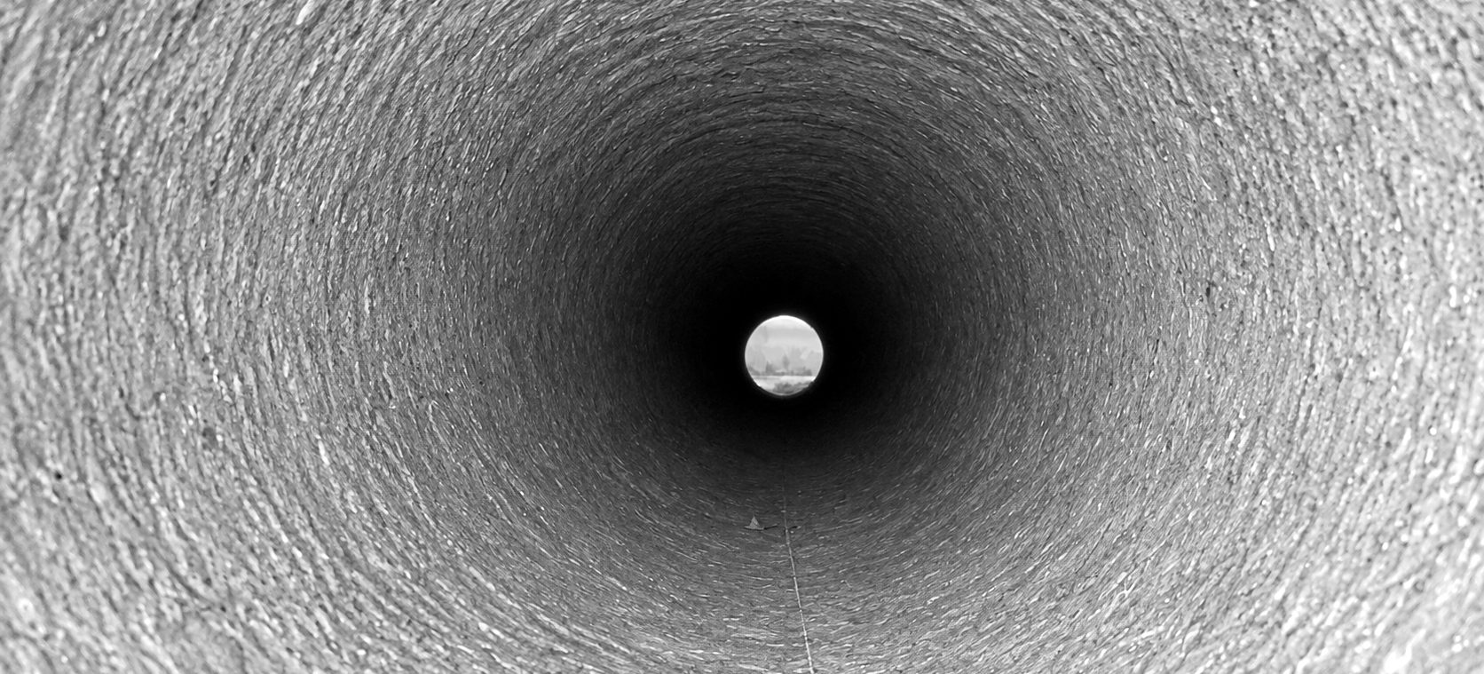 Looking down the inside of a large concrete pipe toward daylight