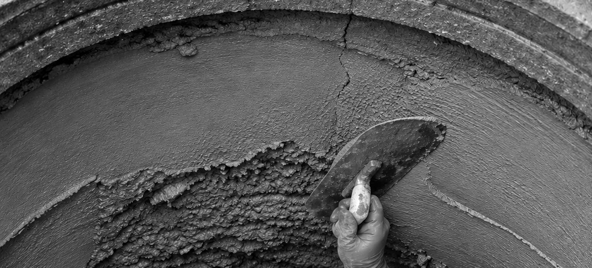 A worker troweling repair mortar onto the inside wall of a manhole