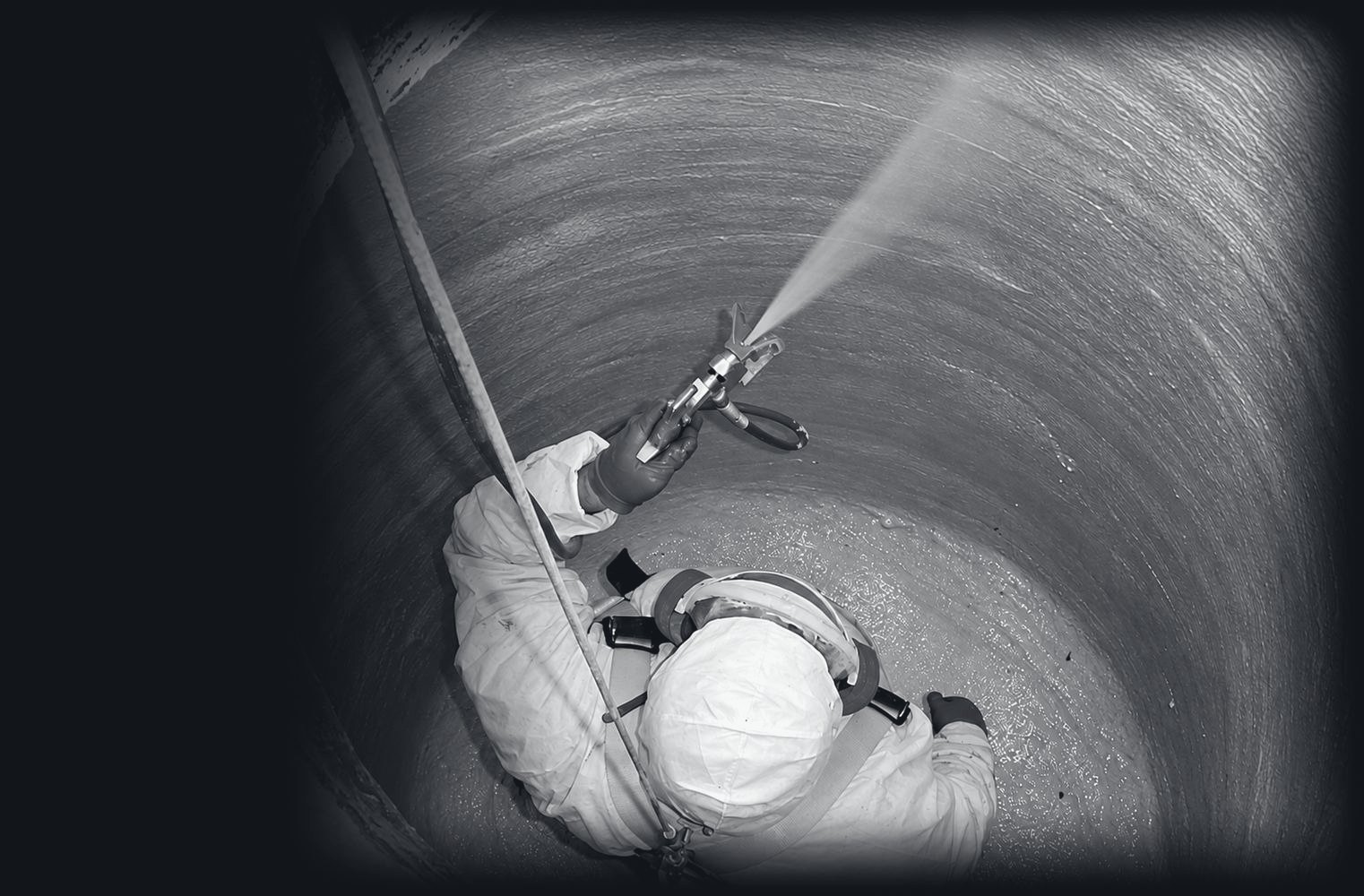 A worker in a harness spraying a cementitious liner onto the inside wall of a manhole