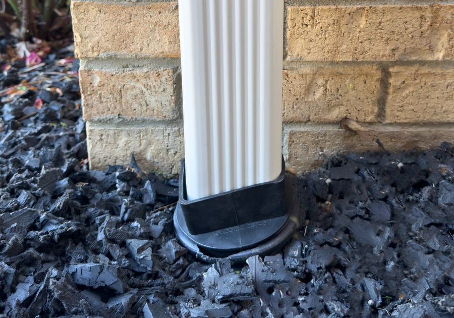 A Fernco downspout connector joining a white downspout to an underground drain line